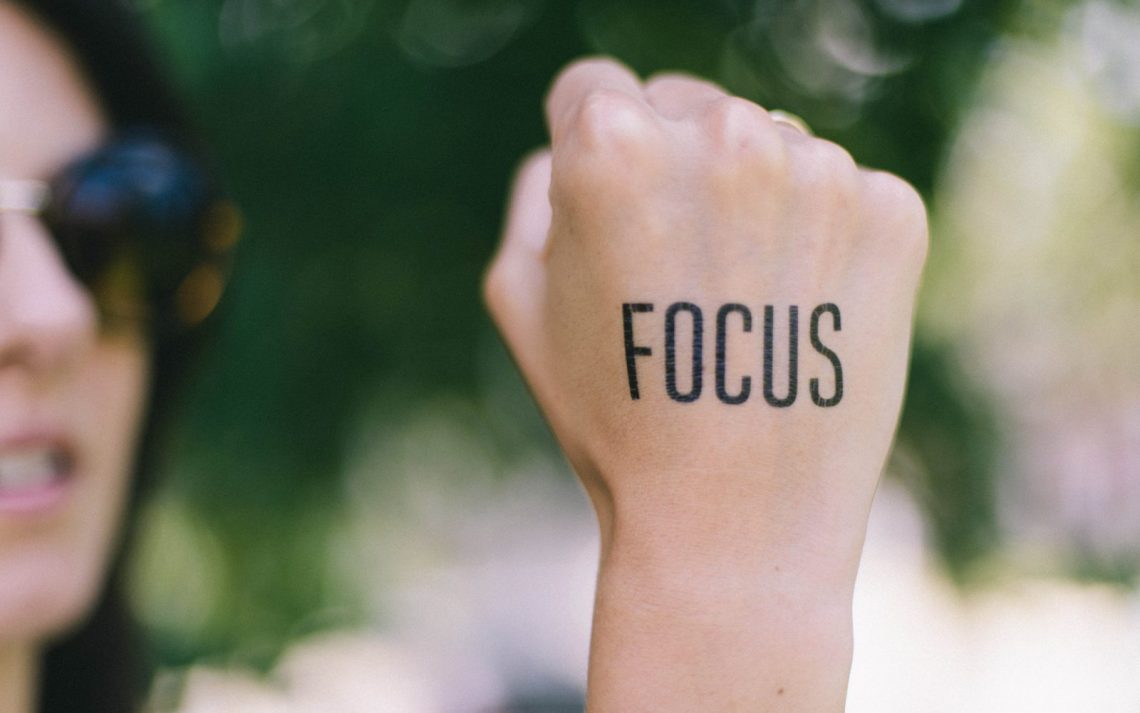 The word "focus" written on the back of someone's fist, with the background blurred.