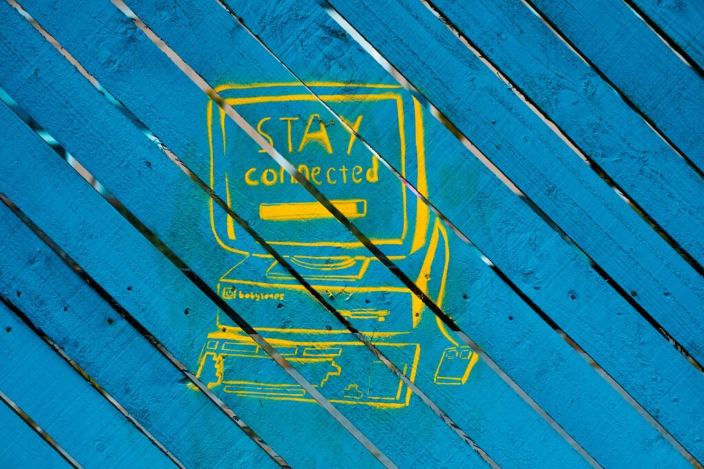 A drawing of a yellow computer with an old CRT monitor that says Stay Connected, on a blue wooden sign.